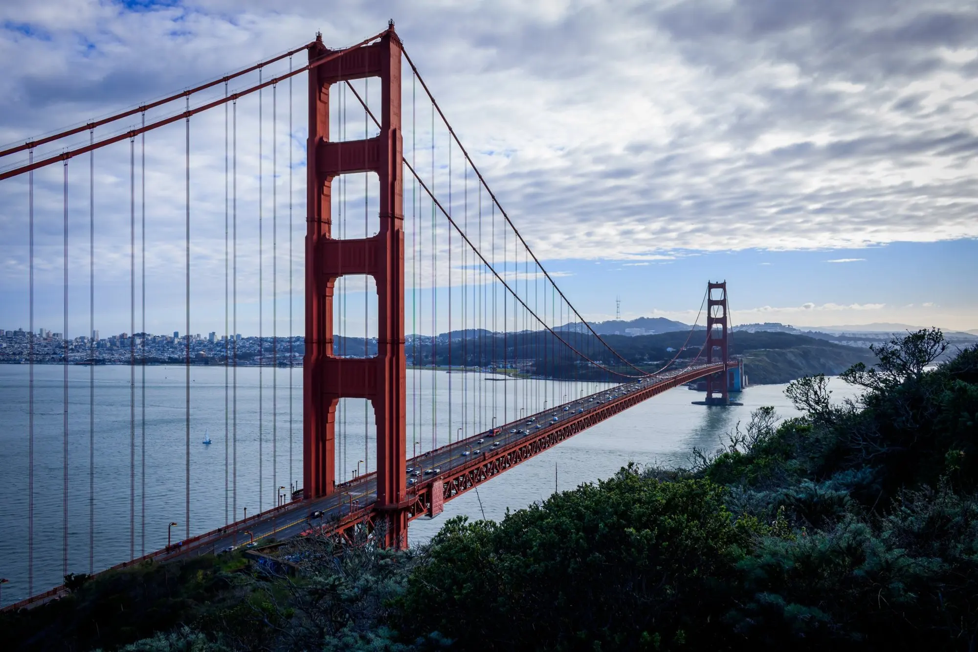 Golden Gate Bridge von einem Hügel aus, dahinter die Bucht und die Stadt unter Wolken